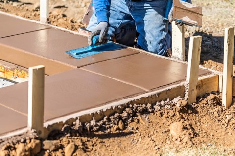 Construction worker using trowel on wet cement forming coping around new pool