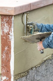 Tile worker applying cement with trowel at pool construction site