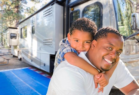 African american father with mixed-race son in front of their beautiful RV at the campground
