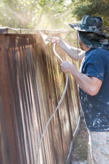 Professional painter spraying house yard fence with wood stain