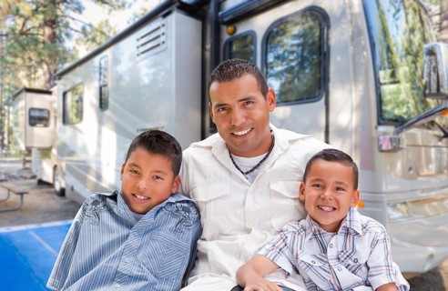 Happy hispanic father and sons in front of their beautiful RV at the campground