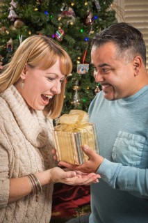 Happy young mixed-race couple with present near christmas tree