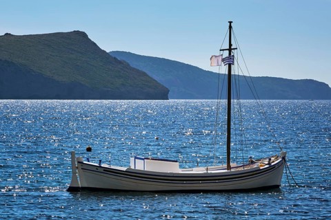 Traditional greek fishing boat in the Aegean sea with greek flag