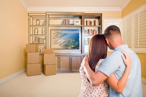 Young military couple looking at drawing of entertainment unit in room with moving boxes