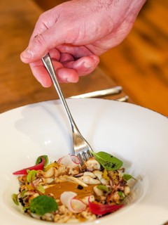 Hand with fork picking from a dish of pan cooked grilled flambe atlantic squid iplated with potato rich sauce cream reduction