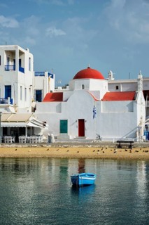 Blue fishing boat in port harbor of Chora town on Mykonos island with orthodox church in background