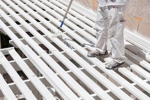 Professional painter rolling white paint onto the top of A home patio cover