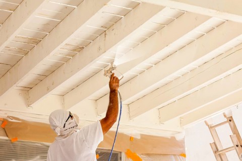 Professional house painter wearing facial protection spray painting deck of A home