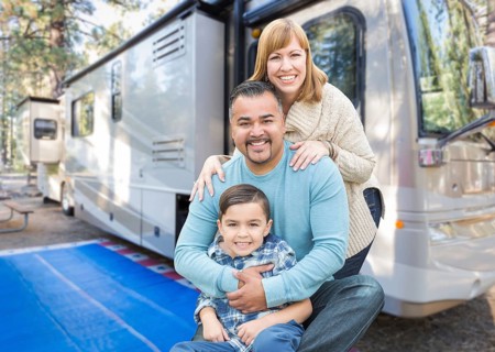 Happy young mixed-race family in front of their beautiful RV at the campground