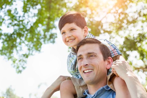 mixed-race father and son playing piggyback together in the park