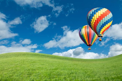 Two hot air balloons up in the beautiful blue sky with grass field below