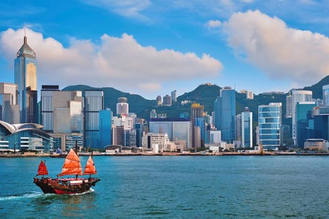 Hong Kong skyline cityscape downtown skyscrapers over Victoria Harbour in the evening with junk tourist ferry boat on sunset with dramatic sky Hong Kong