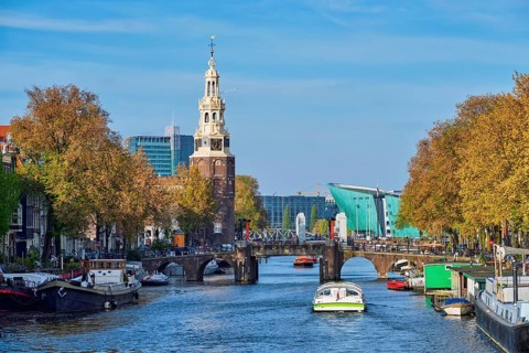 Amterdam cityscape with canal boats and medieval houses and NEMO Science museum and Montelbaanstoren Tower. Amsterdam