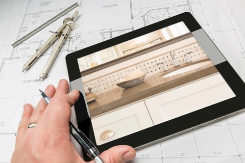 Hand of architect on computer tablet showing luxury bathroom details over house plans