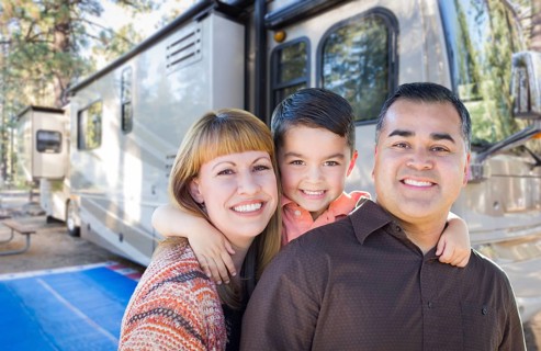 Happy young mixed-race family in front of their beautiful RV at the campground