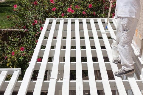 Professional painter rolling white paint onto the top of A home patio cover