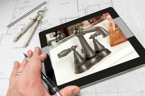 Hand of architect on computer tablet showing luxury bathroom details over house plans