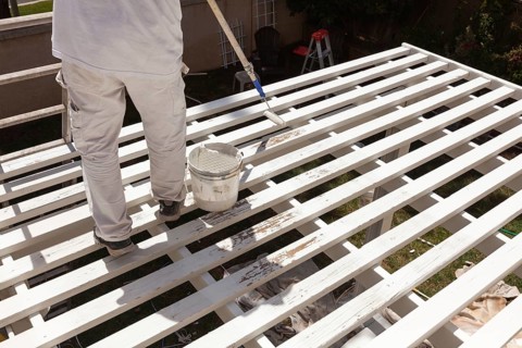 Professional painter rolling white paint onto the top of A home patio cover