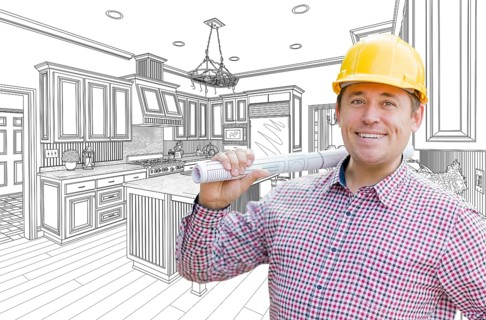 Smiling contractor in hard hat with roll of plans over custom kitchen drawing