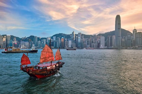 Hong Kong skyline cityscape downtown skyscrapers over Victoria Harbour in the evening with junk tourist ferry boat on sunset with dramatic sky. Hong Kong