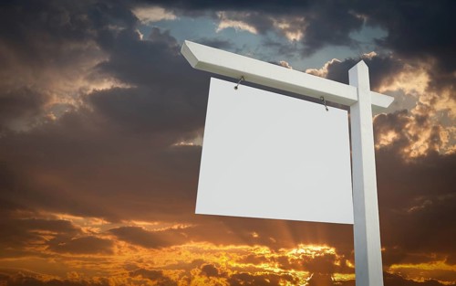 Blank white real estate sign over sunset sky ready for your own message