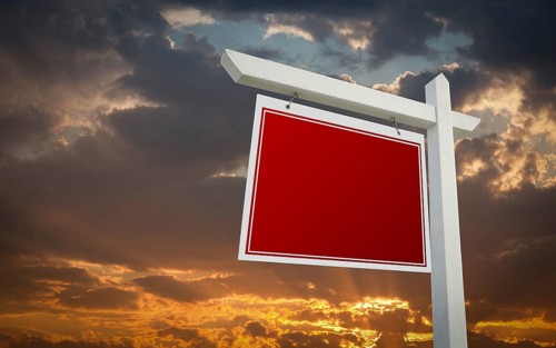 Blank red real estate sign over sunset sky ready for your own message