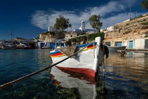 Fishing boats moored in crystal clear turquoise sea water in harbour in Greek fishing village of Mandrakia