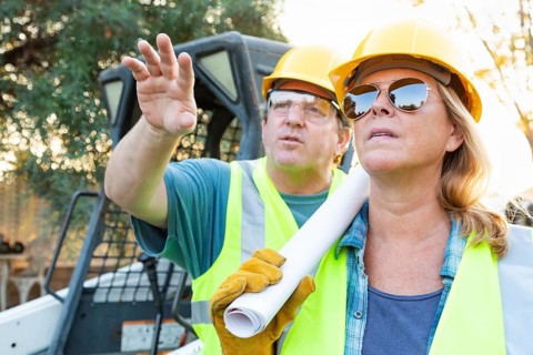 Male and female workers with technical blueprints talking at construction site