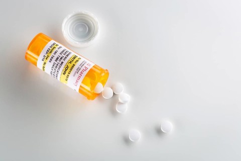 Non-Proprietary medicine prescription bottle and spilled pills over head on grey background