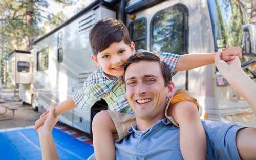 Happy young caucasian father and son in front of their beautiful RV at the campground