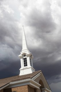 Church steeple tower below ominous stormy thunderstorm clouds