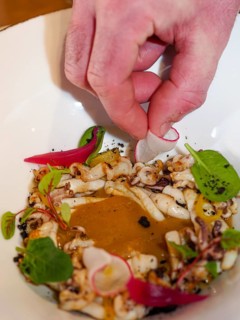 Chef hand close up plating pan cooked flambe atlantic squid with potato rich sauce cream reduction