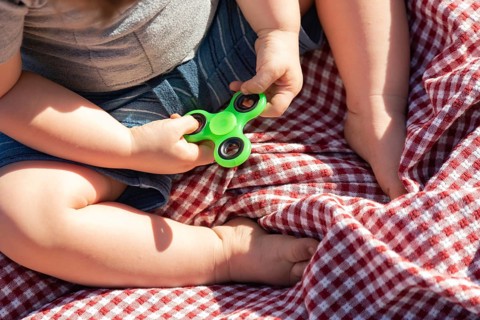 Baby boy sitting on picnic blanket playing with fidget spinner