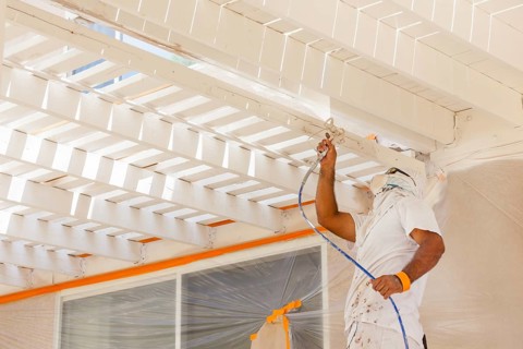 Professional house painter wearing facial protection spray painting deck of A home