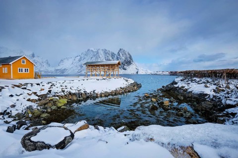 Traditional yellow rorbu house in drying flakes for stockfish cod fish in norwegian fjord in winter Sakrisoy fishing village