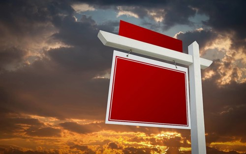 Blank red real estate sign over sunset sky ready for your own message