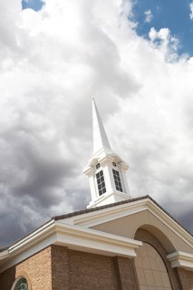 Church steeple tower below ominous stormy thunderstorm clouds