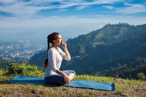 Woman practices pranayama yoga breath control in lotus pose padmasana outdoors in Himalayas in the morning on sunrise. Himachal Pradesh