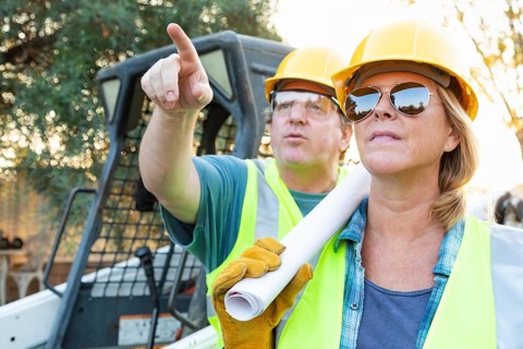 Male and female workers with technical blueprints talking at construction site