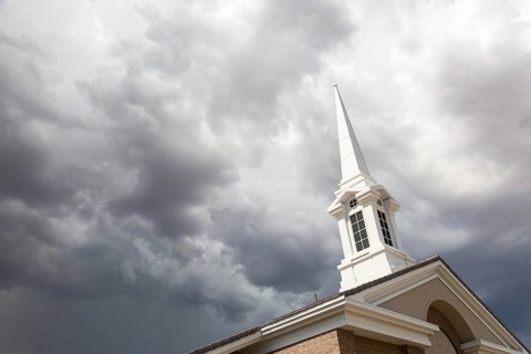 Church steeple tower below ominous stormy thunderstorm clouds