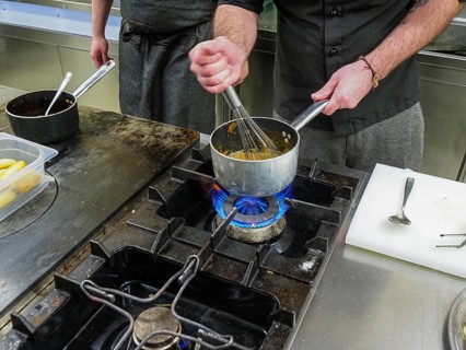 Chef using a hand mixer making a potato sauce cream reduction in a professional kitchen of a restaurant