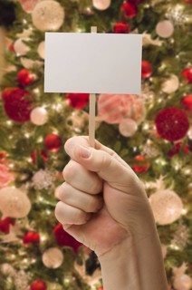 Hand holding blank card in front of decorated christmas tree