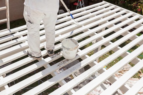 Professional painter rolling white paint onto the top of A home patio cover