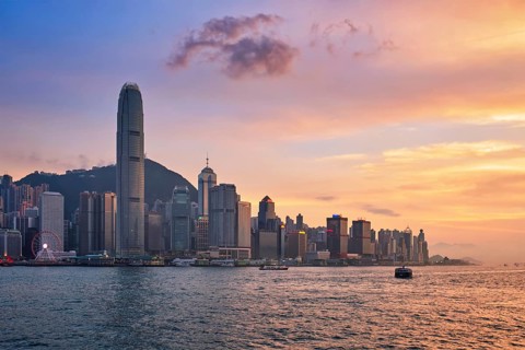 Hong Kong skyline cityscape downtown skyscrapers over Victoria Harbour in the evening with junk tourist ferry boat on sunset with dramatic sky. Hong Kong