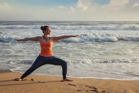 Woman doing Hatha yoga asana Virabhadrasana 1 Warrior Pose outdoors on ocean beach on sunset. Kerala