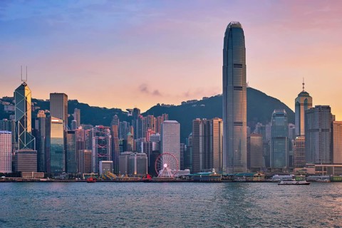 Hong Kong skyline cityscape downtown skyscrapers over Victoria Harbour in the evening with junk tourist ferry boat on sunset with dramatic sky. Hong Kong