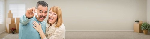 Young adult couple inside room with boxes holding new house keys banner