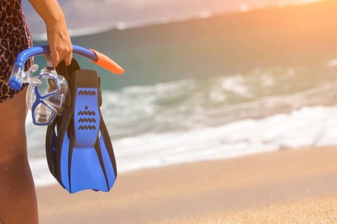 Woman holding snorkeling gear on the shoreline