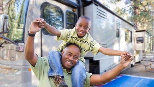 Happy african american father and son in front of their beautiful RV at the campground