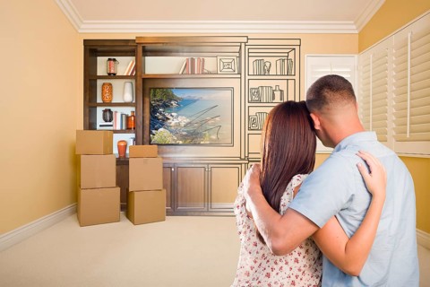 Young military couple looking at drawing of entertainment unit in room with moving boxes